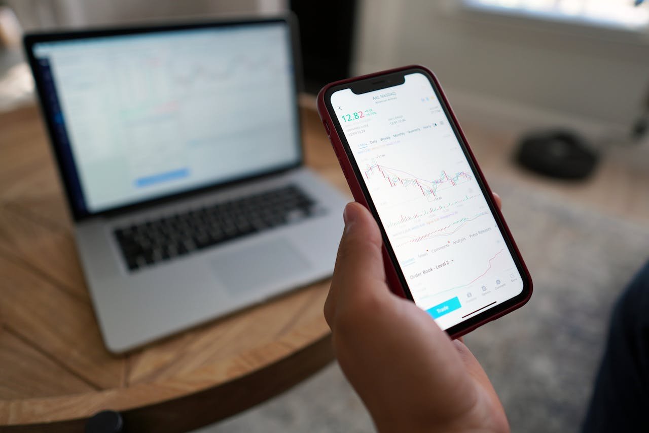 A person trading stocks on a smartphone and laptop. Ideal for finance themes.